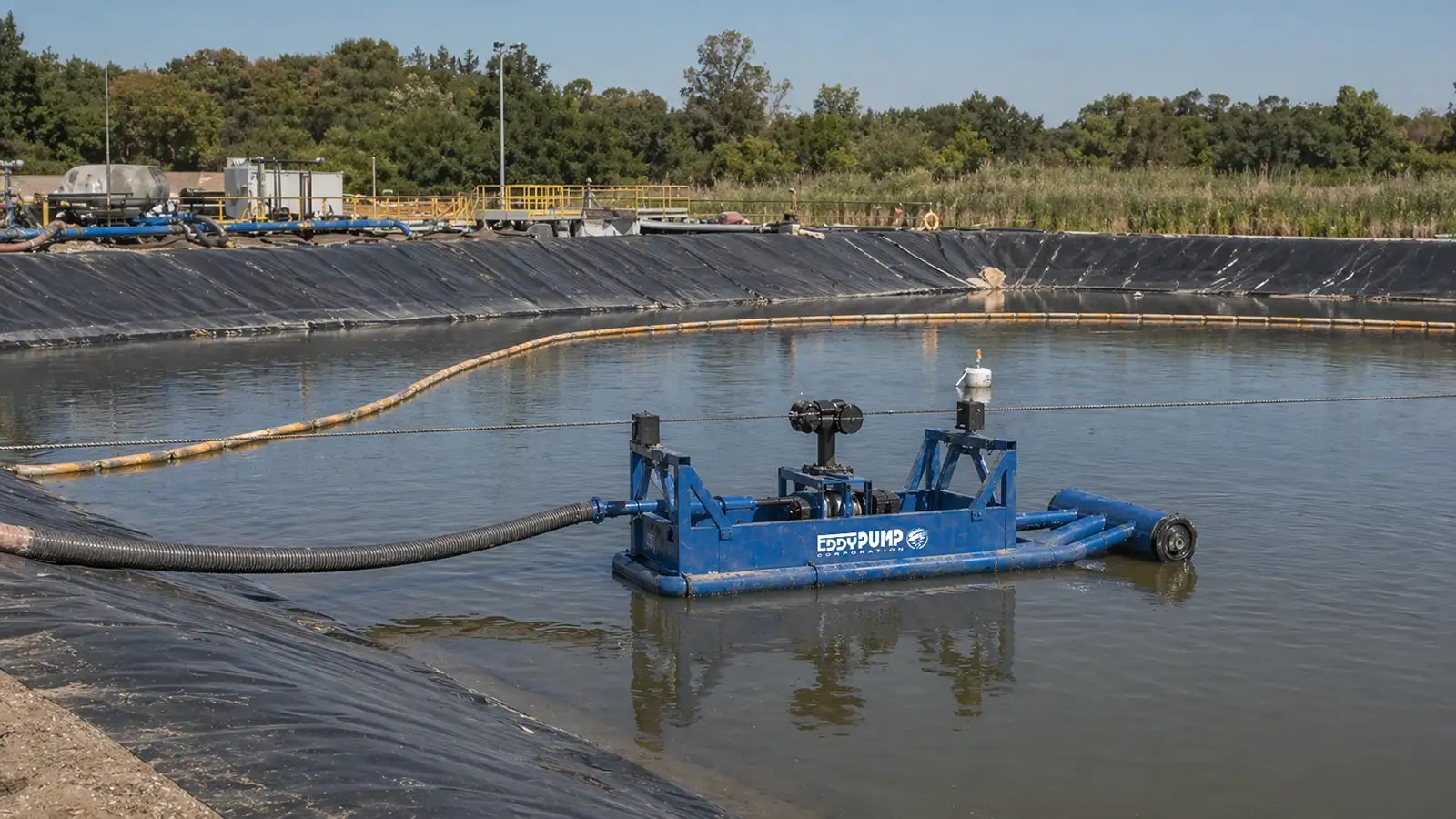 Skid-mounted floating dredge working an HDPE-lined containment pond, with a floating discharge line resting on the liner to protect it from damage.