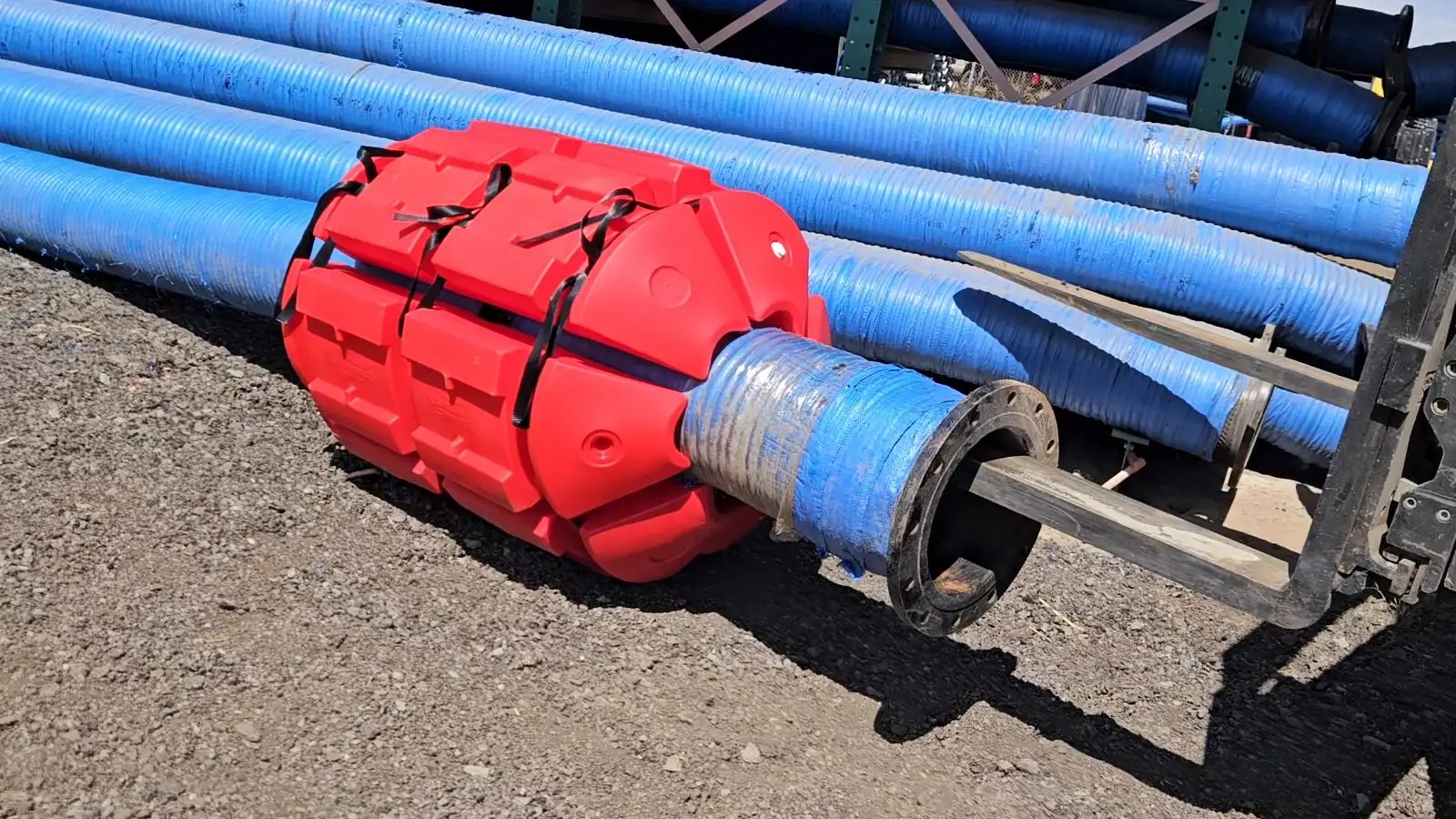 Red pipeline float fitted around a flanged dredge discharge hose, with blue slurry hoses stacked behind