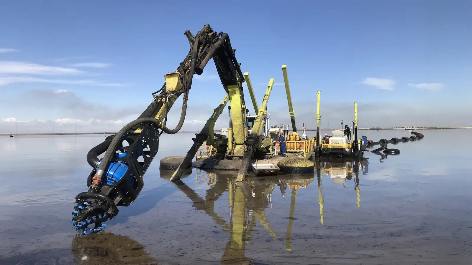 Excavator-mounted dredging attachment positioned on a floating platform for material removal and pumping
