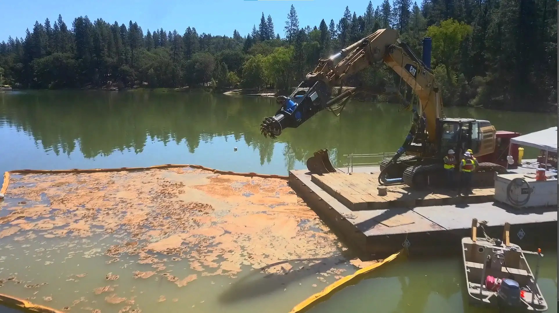 Excavator hydraulic attachment operating from a floating work platform in a lake dredging project