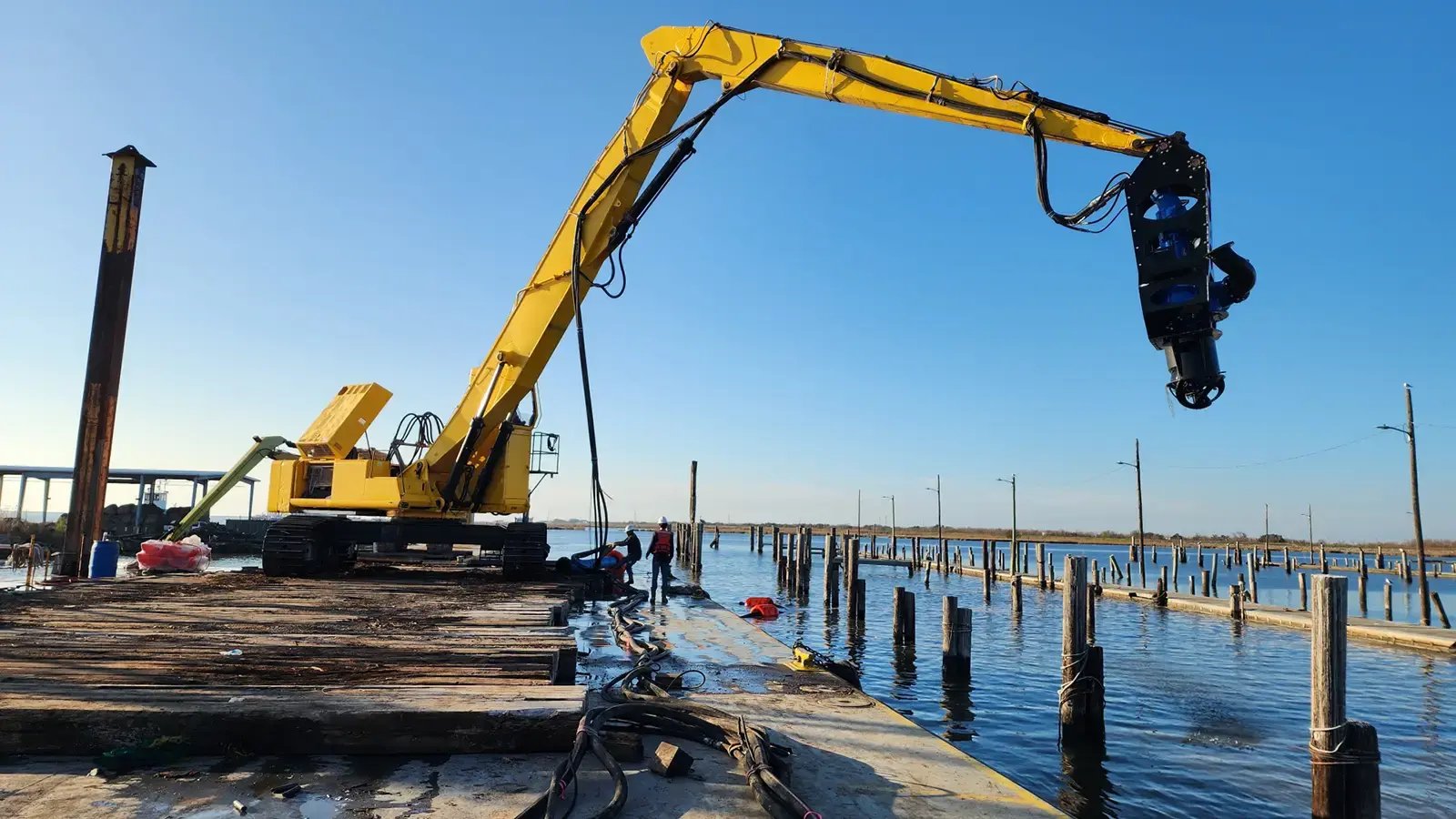 Long-reach excavator on a barge holding an EDDY Pump excavator dredge pump attachment over the water