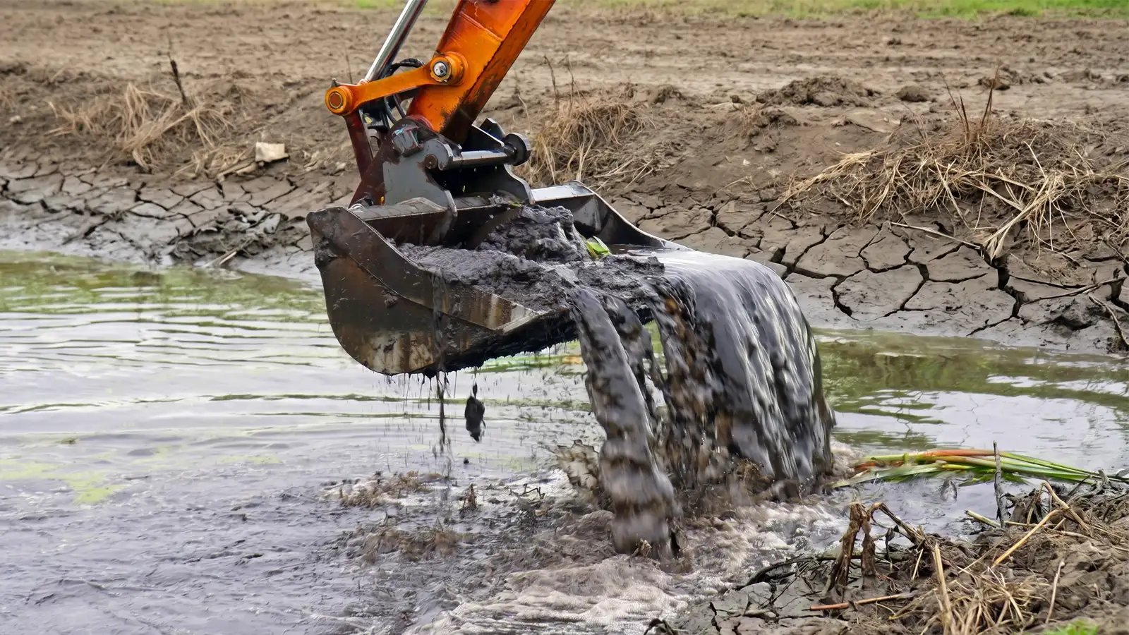 Excavator bucket removing wet mud and sediment from a canal during dredging and cleaning work